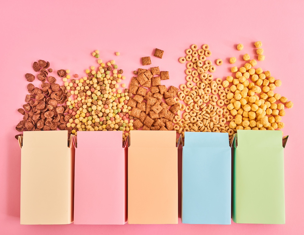 Colorful boxes of cornflakes or cereal of different types on pink background, top view